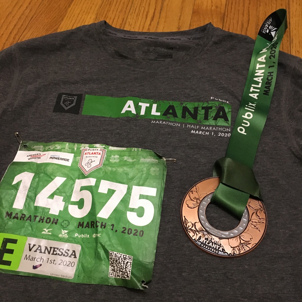 Race bib and finisher medal shown on top of gray Publix Atlanta Marathon race shirt.