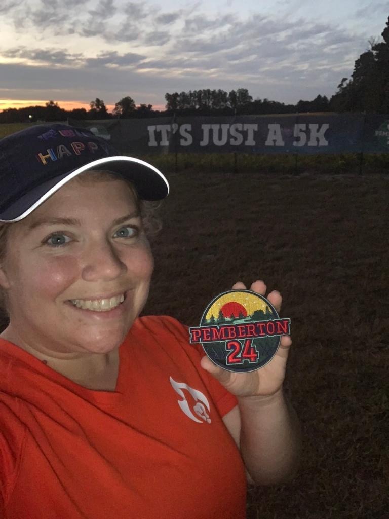 Vanessa Junkin holds Pemberton 24 patch in front of "It's Just a 5K" banner. 