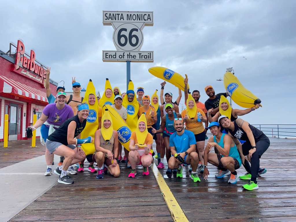 A group of runners, many dressed in banana outfits, pose by a sign that says "Santa Monica 66 End of the Trail." 