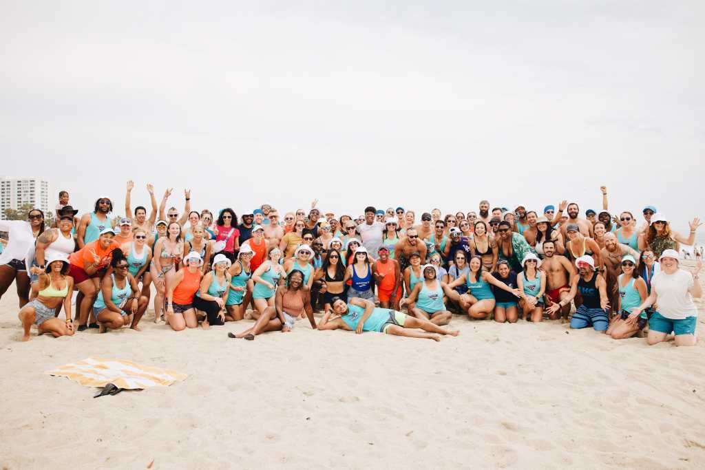 A large group of people pose for a photo on the beach. 