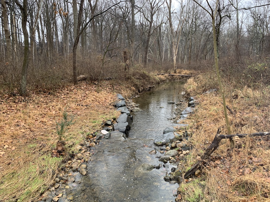 Waterway with rocks on both sides shown in the woods in the winter. 