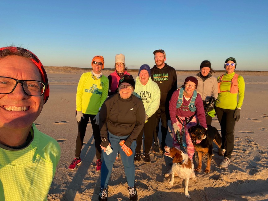 Nine runners and two dogs pose for a photo on the beach. 