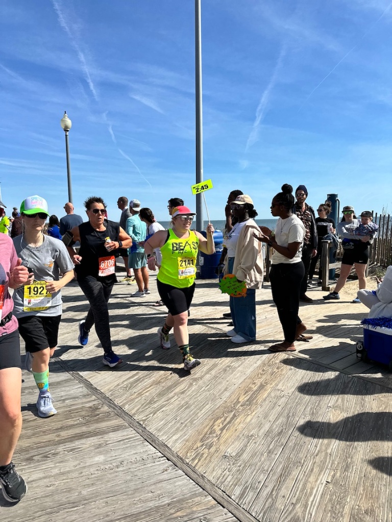 Vanessa Junkin, in neon yellow Beast Pacing tank and holding sign, runs on the boardwalk near the finish of the Coastal Delaware Running Festival Half Marathon.