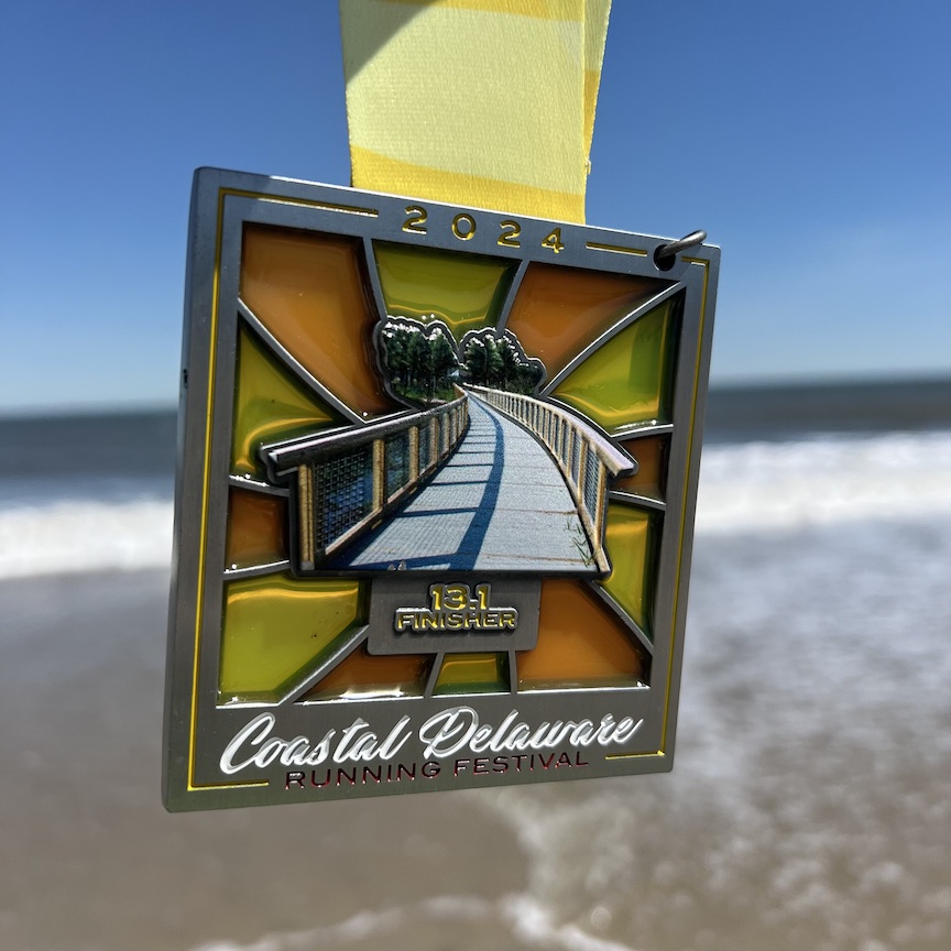 Finisher medal for the Coastal Delaware Running Festival Half Marathon against the backdrop of the beach. 
